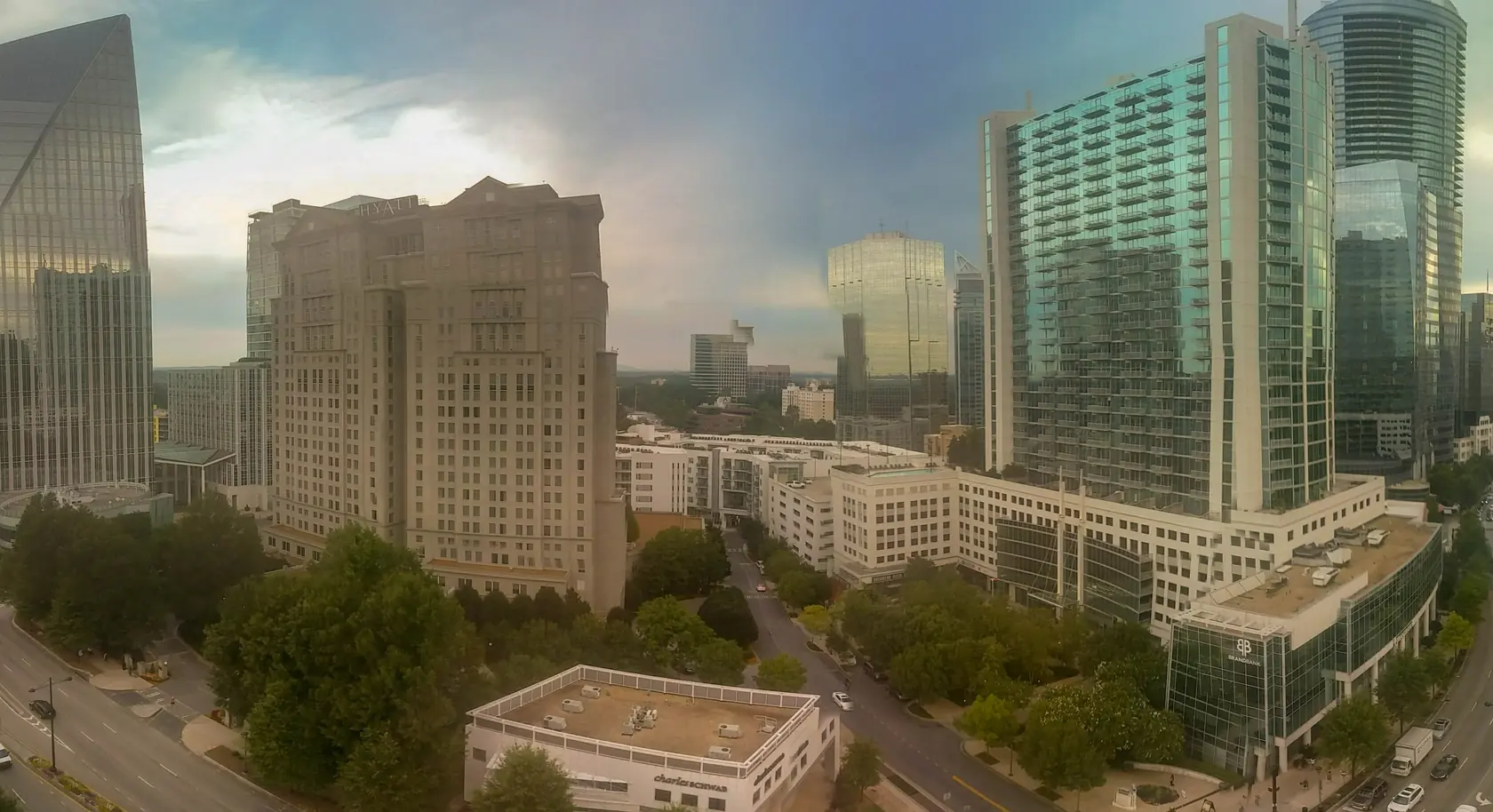 A tree-lined multi-lane boulevard running between stone and glass towers under a grey-blue storm sky with a bright break in the clouds.