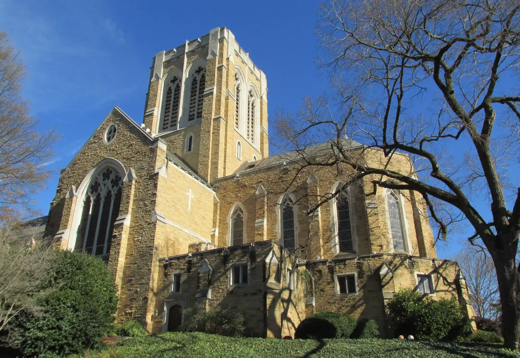 A Gothic Revival cathedral in warm tan stone with a square bell tower and a large traceried window, above a slope of ivy, against a deep blue winter sky.